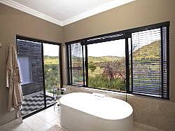 Luxury bathroom with freestanding tub and scenic bushveld view at Shepherd’s Tree Game Lodge in Pilanesberg Reserve, South Africa.